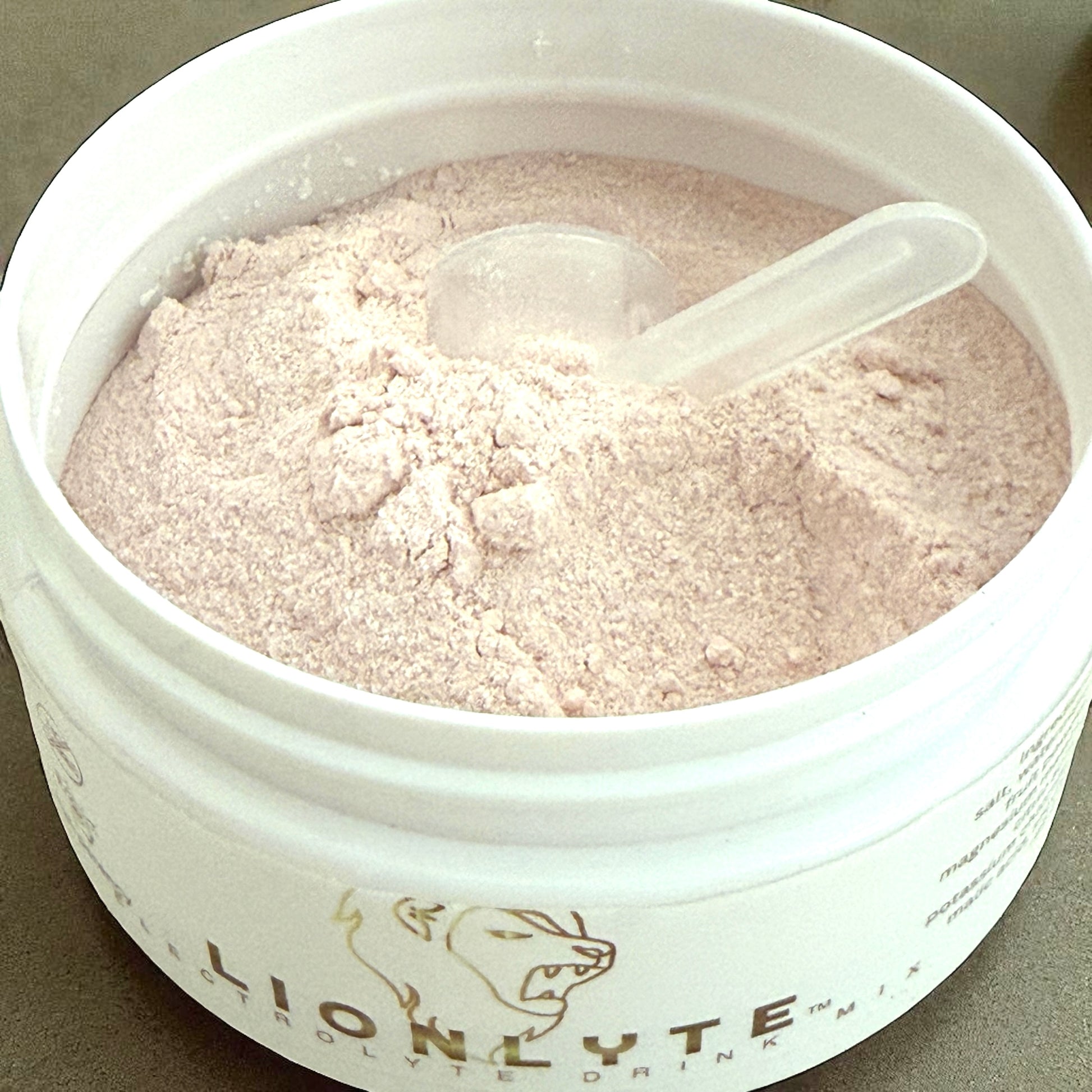Container of Lionlyte drink mix with a spoon inside on a gray background